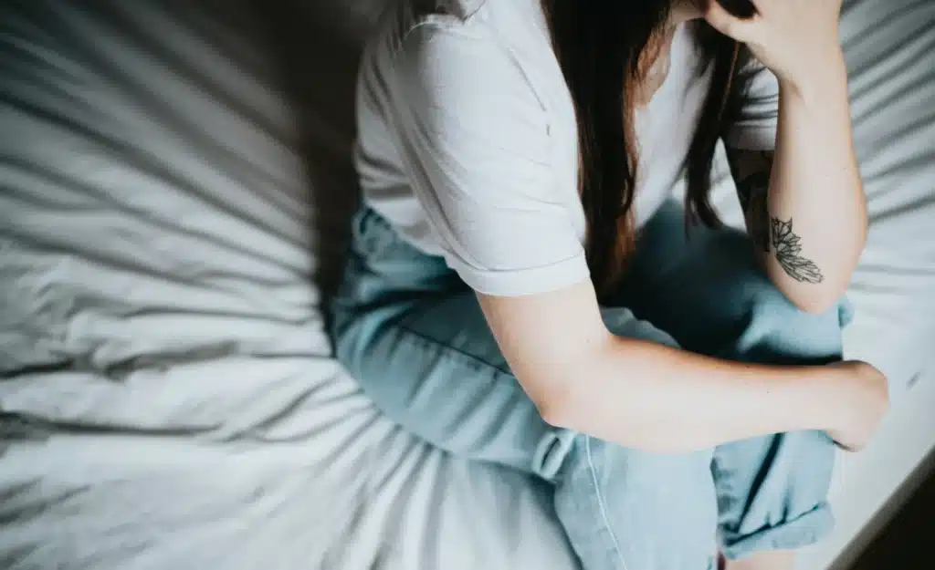 Woman sitting on bed considering treatment for self-harm scarring in Devon